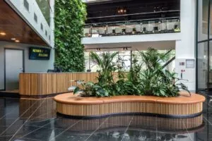 Moderne ontvangsthal van het John M. Keynesplein met houten receptiebalie, groene plantenwand en ronde zitbank met planten.